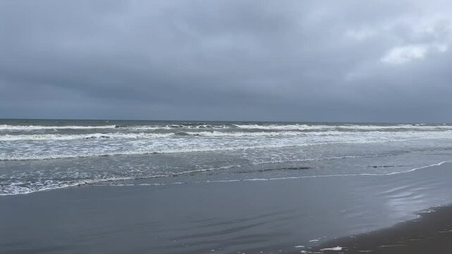 Fast moving alone grey sand beach coastline with waves and cloudy sky 