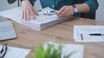 Businessman or auditor wearing green shirt is reviewing financial documents with magnifying glass....
