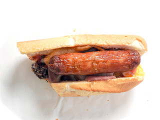 Traditional Irish breakfast roll with cooked sausages, bacon or rashers and black and white pudding in a round bread on light color paper. Popular meal with high calorie count.
