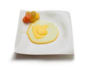 Condensed milk and custard desert looks like a fired egg and colorful jelly sweets in sugar on a white fancy square plate and light background. Creative food ideas. Light and airy look