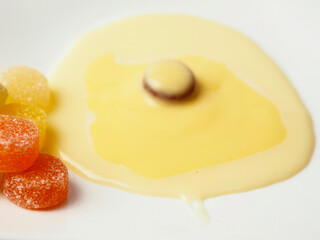 Condensed milk and custard desert looks like a fired egg and colorful jelly sweets in sugar on a white fancy square plate and light background. Creative food ideas. Light and airy look