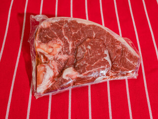 Fresh uncooked T bone steak in plastic wrap on classic red and white stripe table cloth. High...