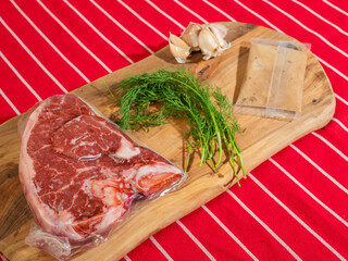 Fresh uncooked T bone steak with fresh dill and garlic clove and sauce in a plastic pouch on...