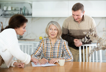 Competitive middle-aged man and woman conflicting and old woman writing inheritance sitting at...