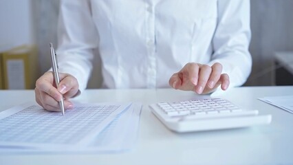 Businesswoman with white blues calculating finance with calculator and taking notes at office table. Audit and taxes