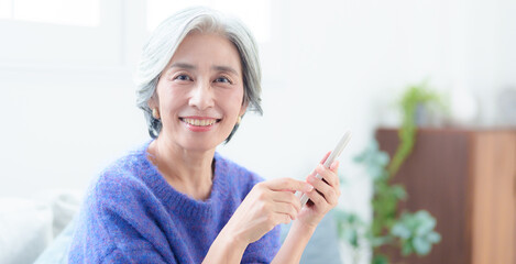 Fototapeta premium リビングでスマートフォンを使う中高年の女性