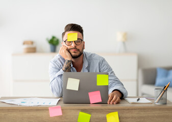 A lot of work concept. Tired freelancer man sleeping at workplace with stickers on foehead and computer, working on laptop at home office, sitting at table in living room, free space