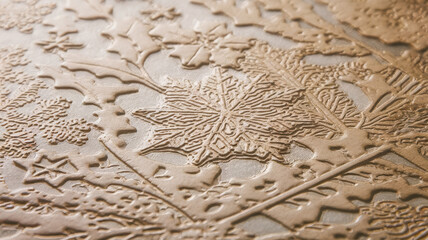 Close-up of an intricately embossed metallic surface featuring leaf and snowflake designs, showcasing details in rich, warm tones.