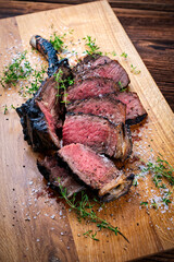 Traditional grilled barbecue dry aged tomahawk beef steak meat with salt and fresh herbs served and sliced as close-up on a wooden design board