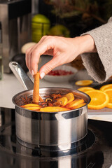 A woman adds a stick of cinnamon to the boiling mulled wine in a saucepan in the kitchen. 
