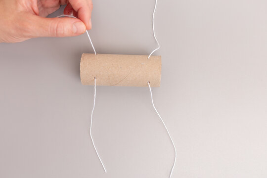 pair of hands working with empty toilet paper roll, threading a string through holes, step in creative process,