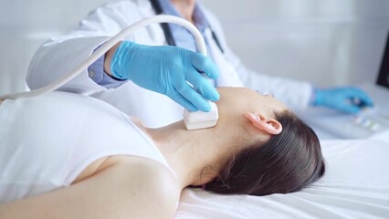Doctor man wearing blue medical gloves is using ultrasound equipment on neck of female patient lying down for a medical examination