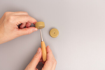pair of hands working with two round, beige plastic caps. create a hole in the center of the cap....