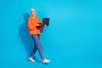 Photo of walking old lady worker using netbook for coworking distance wear jean pullover isolated blue color background