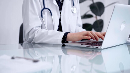 Doctor woman is typing on laptop computer at glass table in clinic, horizontal view. Medicine and pharmacy concept