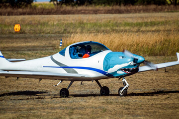 A small plane with a spinning propeller is ready to take off from dry grass