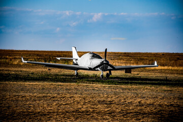 A small covered airplane stands in a field against the sky