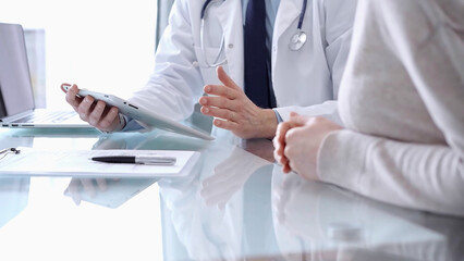 Doctor is consulting patient in modern clinic. Healthcare professional discusses medical information with a woman, using a tablet computer. Medicine concept