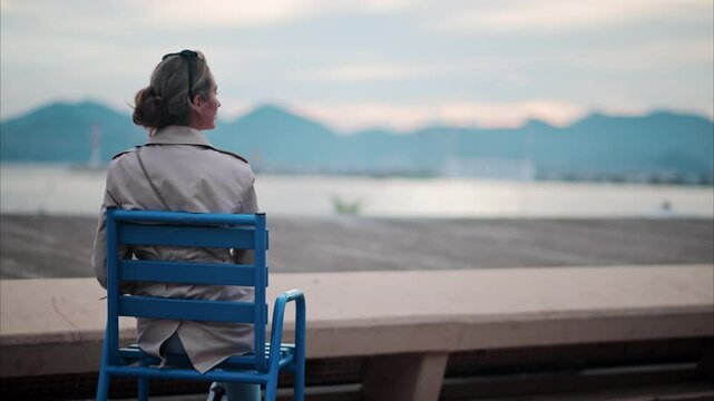 Woman in a trench coat sitting on a chair at the beach in France