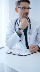 Doctor and a patient. The physician, wearing a white medical coat over a green shirt, gesturing with his hands during a consultation in the clinic. Medicine concept