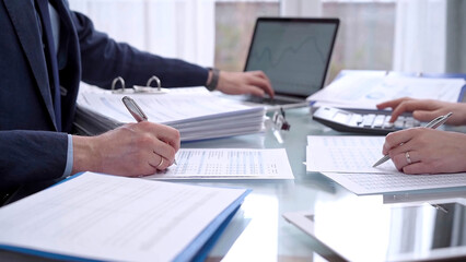 Business people wearing blue suits are reviewing financial data in office. Two professionals...