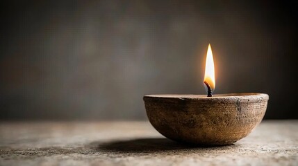 A single candle flame burns brightly in a rustic clay bowl, casting a warm glow against a dark background.