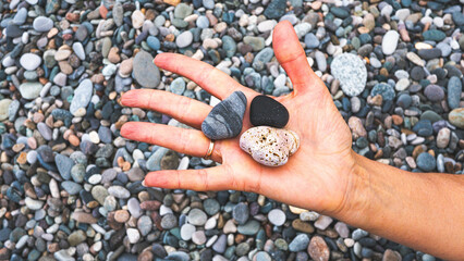 Woman hand holding a stone on a pebble beach feminine