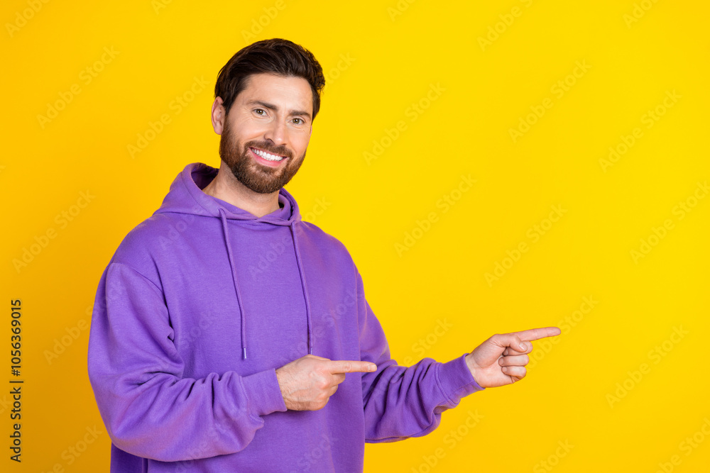 Poster portrait of good mood man with stylish bristle dressed purple hoodie indicating at sale empty space 