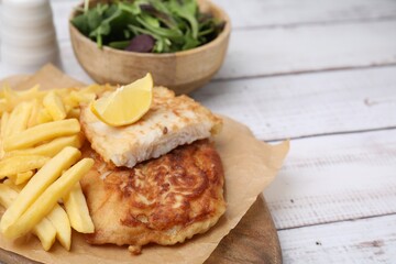 Tasty soda water battered fish, potato chips and lemon slice on white wooden table, space for text