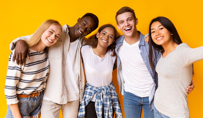 Friendly international group of teenagers embracing and taking selfie over yellow background