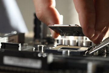 Man installing computer chip onto motherboard at table, closeup