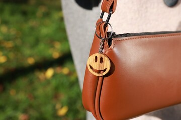Stylish bag with wooden keychain in shape of smiley face outdoors, closeup. Space for text
