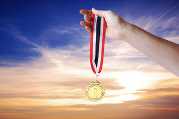 Woman holding gold medal in hand against sunset sky, closeup