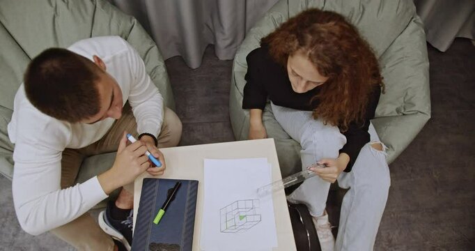 Two college students studying geometry together in comfortable beanbag chairs after class. They discuss formulas and practice problem-solving, showcasing teamwork and focused learning.