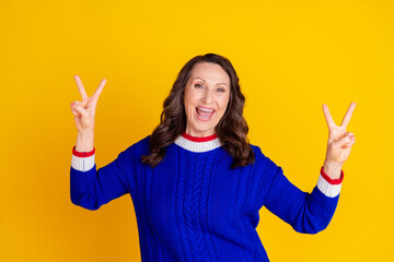 Photo portrait of lovely pensioner lady show v-sign dressed stylish blue knitted garment isolated on yellow color background