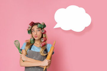 Pensive housewife presses lips for kiss and looks up, rolling pin and whisk in hands