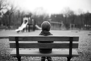 Emotionally neglected child sitting alone on a park bench, with an empty playground in the background