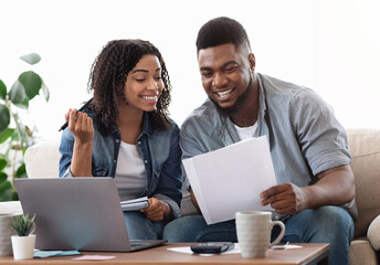 Happy black couple reading financial documentation at home while planning family budget together,...