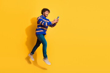 Full body photo of attractive young man running hold device dressed stylish blue striped clothes isolated on yellow color background
