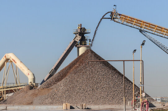 Aggregate processing facility with conveyor systems depositing crushed stone into a large stockpile, illustrating industrial material handling and construction supply chain infrastructure