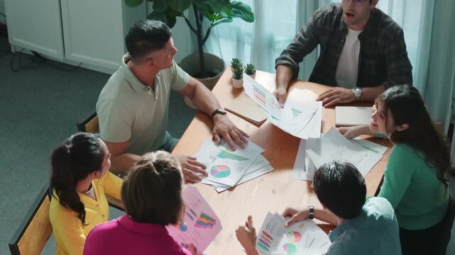 Top view of smart people throw paper and giving high five at meeting table with financial document and stock market analysis paper scattering around. Aerial view of team celebrate project. Symposium.