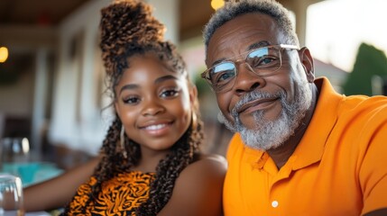 An older man with glasses and a beard smiling next to his granddaughter, both in vibrant orange shirts, capturing a moment of familial joy and togetherness.
