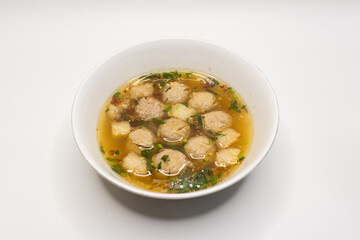Bowl of Indonesian meatball soup with savory broth, meatballs, and garnish. Traditional Indonesian food served in a white bowl.