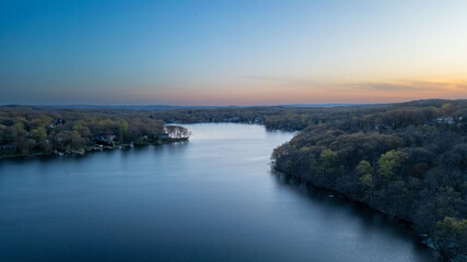 Obraz premium Tranquil sunset over a serene lake, capturing the peaceful reflections of fading sunlight on calm waters with silhouetted trees on the shoreline.