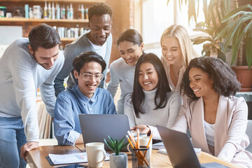 Friendly young international team looking at laptop screen, watching business presentation at office