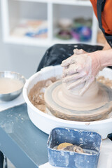 Close-up of a potter's hands working on a pottery wheel. Vertical photo. 