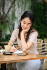 Happy woman resting her hand on chin while writing