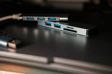 A compact, gray USB-C hub with multiple ports and attached cables, resting on a metallic surface...