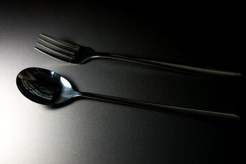 A metallic fork and spoon, side by side, positioned horizontally on a flat surface, reflecting...