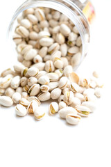 An open container of pistachios tipped over, spilling the nuts onto a white surface. The pistachios, in their partially open shells, showcase the vibrant green nuts inside, highlighting texture and co